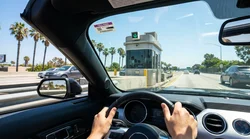 White car rental driving on a Los Angeles freeway under an overhead electronic toll sign