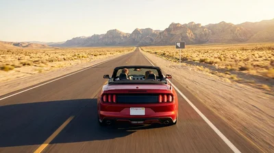 White car rental driving on a sunny desert highway in California with mountains in the distance