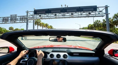 White car rental driving under an electronic toll gantry on a sunny Florida highway