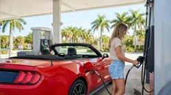 Fuel pump nozzle inserted into a white car rental vehicle at a sunny Miami gas station