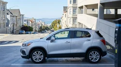 A white car rental parked next to a street meter on a steep hill in San Francisco