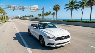 A white convertible car hire driving along Ocean Drive in Miami with palm trees and Art Deco hotels