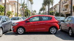 Small white car rental driving past palm trees on a sunny Los Angeles street