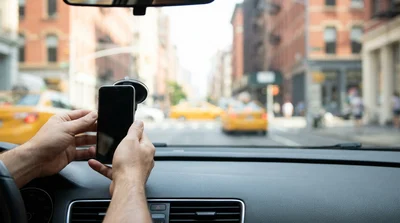 Smartphone mounted on a dashboard phone holder inside a car rental parked on a New York street