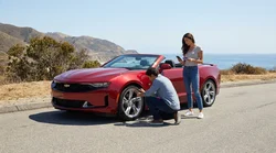 Driver inspecting a flat tyre on a car rental parked on the shoulder of a highway in California