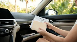 Hands placing paperwork into the open glovebox of a Florida car rental parked under palm trees