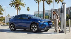 Driver using a smartphone next to a plugged-in electric car rental at a sunny California charging station