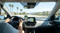 Smartphone displaying a navigation map mounted on the dashboard of a car rental on a scenic California highway