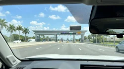 Silver car rental passing through an electronic toll plaza on a sunny Florida highway