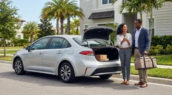 Person putting food delivery bags into the trunk of a car rental on a sunny palm-lined street in Florida