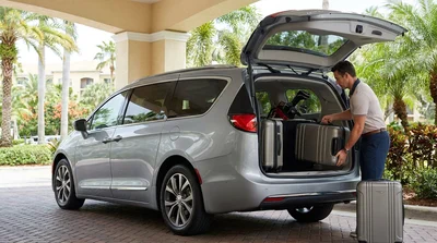 Golf clubs and suitcases packed into the open trunk of a car rental parked near palm trees in Florida