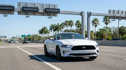 White car hire passing under an electronic toll gantry on a sunny Florida highway