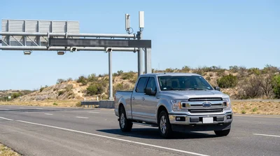 White car rental driving on a sunny Texas highway approaching a toll gantry