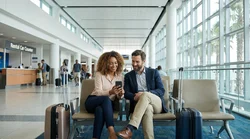 Traveler with luggage using a smartphone beside a car rental vehicle at LAX in Los Angeles