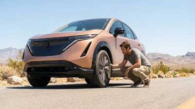 Person checking the tire and underbody of a white car rental parked on a bright Las Vegas street