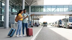 Travelers waiting with luggage at a car hire shuttle stop outside Newark Terminal B