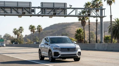 A modern car rental driving on a sunny California highway approaching a toll plaza