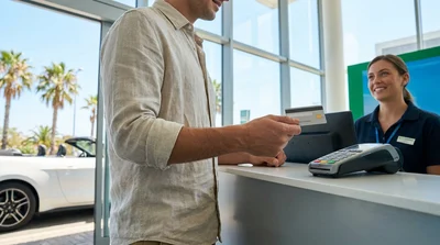 Close-up of a person holding a credit card and keys at a Florida car rental counter