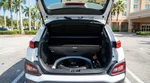 Open trunk revealing a spare tyre in a white car rental parked under palm trees on a sunny Miami street