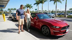 Smiling couple driving a white car rental along a sunny palm tree lined road in Florida