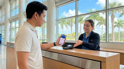 Customer holding a smartphone over a payment terminal at a Florida car rental counter