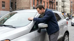 Driver inspecting the windscreen and mirrors of a car rental parked on a New York street