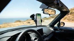 Smartphone attached to a windscreen mount inside a car rental facing a sunny California highway