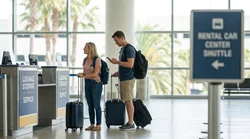 Traveler standing with luggage next to a car rental vehicle in Los Angeles