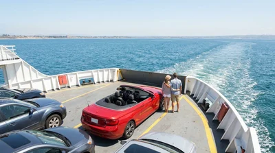 A parked car rental on an open ferry deck overlooking the ocean and the scenic California coastline