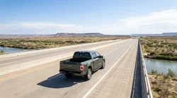 A white car rental driving past a Welcome to Texas state line sign on a desert highway