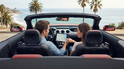 White car rental driving on a scenic coastal highway in California under a clear blue sky