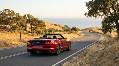 A sleek car rental driving along the Pacific Coast Highway next to the ocean in California