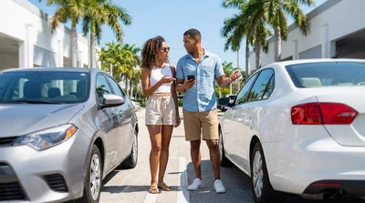 A silver mid-size sedan for car hire parked along a sunny beach with palm trees in Miami