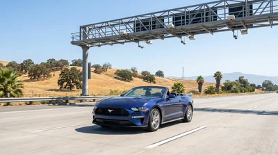 Rear view of a silver car rental passing under an electronic toll gantry on a California highway