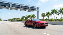 Silver car rental passing through a highway toll plaza on a sunny day in Florida