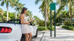 Person holding a smartphone inside a parked car rental on a sunny Florida street