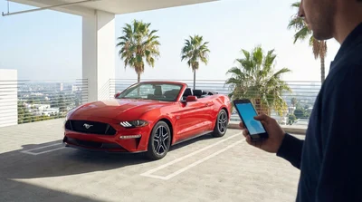 Person tapping a smartphone screen next to a parked car rental on a sunny Los Angeles street