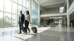 Travelers with luggage walking through the Brightline train terminal in Orlando toward the car rental desks