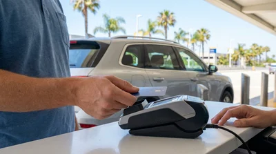Customer tapping a contactless credit card on a payment terminal at a California car hire desk