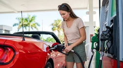 Person pumping fuel into a white car rental at a sunny gas station in Florida