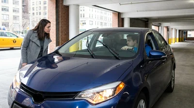 Driver inspecting the illuminated headlights of a car rental parked on a New York street