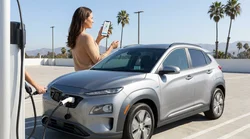 Person plugging a charging cable into an electric car rental at a sunny public station in California