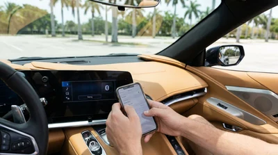 Driver's hands pairing a phone to a car rental dashboard screen with a sunny Miami street seen through the windshield