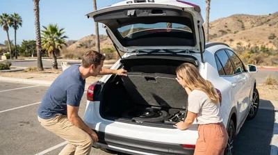 Person inspecting the open trunk of a car rental parked on a sunny scenic road in California