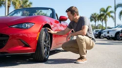 Person kneeling to check a tyre on a car rental vehicle in a sunny Florida parking lot