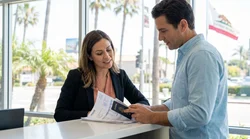 Customer handing documents to an agent at a car rental desk in California