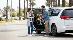 Parent fastening a child seat inside a car rental parked on a sunny California street