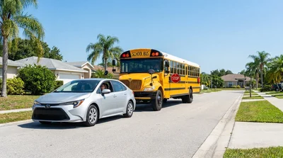 White car rental stopped behind a yellow school bus with its stop sign extended on a Florida road
