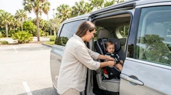 A young child safely buckled into a car seat in the back of a Florida car rental on a sunny day