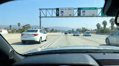 White car rental driving in the HOV lane of a busy Los Angeles freeway with overhead signs